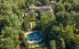 Aerial view of a luxurious villa surrounded by lush greenery, featuring a serene swimming pool and sun loungers in a tranquil garden setting. Perfect for relaxation and outdoor gatherings.