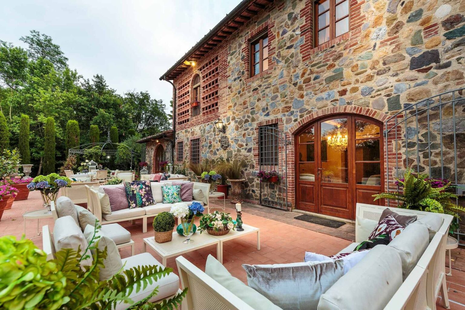 Charming outdoor patio with stone house, featuring comfortable seating, lush greenery, and decorative plants, ideal for relaxation and gatherings. | Only on SopranoVillas