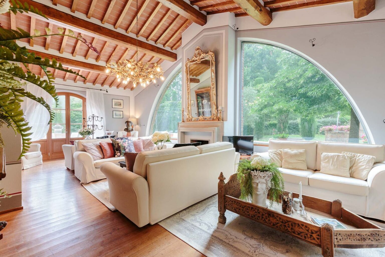 Spacious living room with high wooden ceiling, large windows overlooking greenery, elegant furniture, and decorative accents, creating a warm and inviting atmosphere. | Only on SopranoVillas