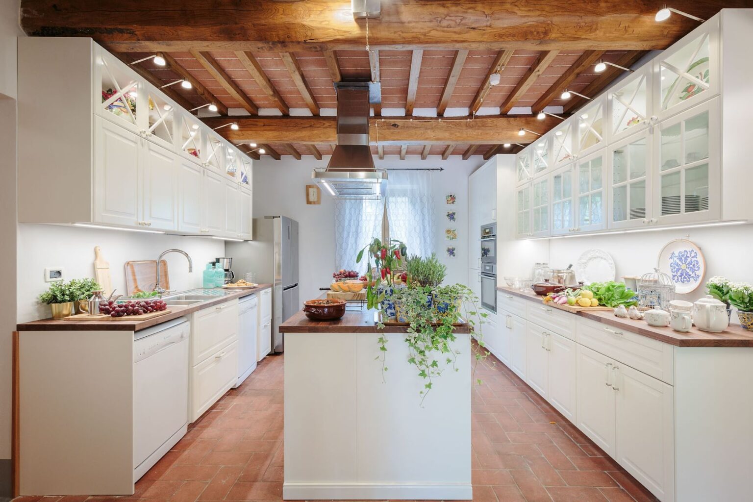Bright and modern kitchen featuring white cabinetry, wooden beams, and a spacious island with plants and fresh produce, designed for functionality and style. | Only on SopranoVillas