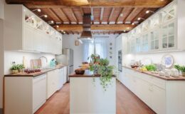 Bright and modern kitchen featuring white cabinetry, wooden beams, and a spacious island with plants and fresh produce, designed for functionality and style.