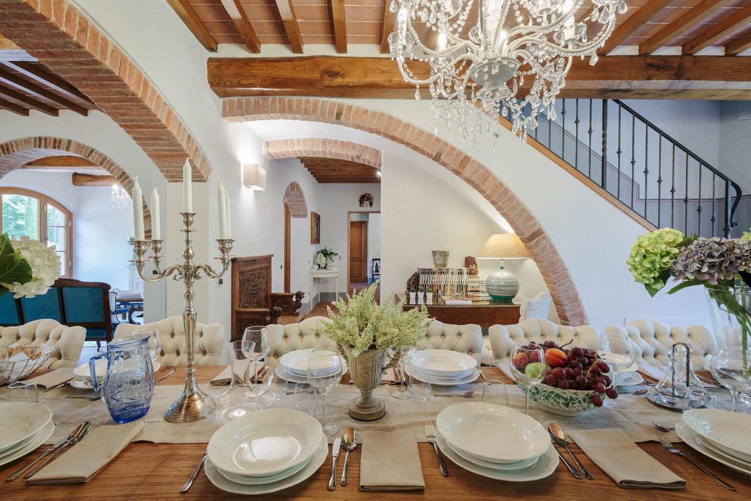 Elegant dining room featuring a beautifully set table with fine china, crystal glassware, and fresh flowers. The room's rustic charm is highlighted by wooden beams, a vintage chandelier, and an inviting atmosphere. | Only on SopranoVillas