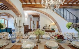 Elegant dining room featuring a beautifully set table with fine china, crystal glassware, and fresh flowers. The room's rustic charm is highlighted by wooden beams, a vintage chandelier, and an inviting atmosphere.