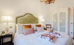 Cozy bedroom featuring a plush green headboard, decorative pillows, stylish bedside lamps, and an elegant wardrobe, creating a warm and inviting atmosphere.