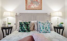 Cozy bedroom featuring a light-colored bed with decorative pillows in green and pink hues, flanked by stylish nightstands with lamps. A colorful zebra-themed artwork hangs above the bed, enhancing the room's aesthetic appeal.