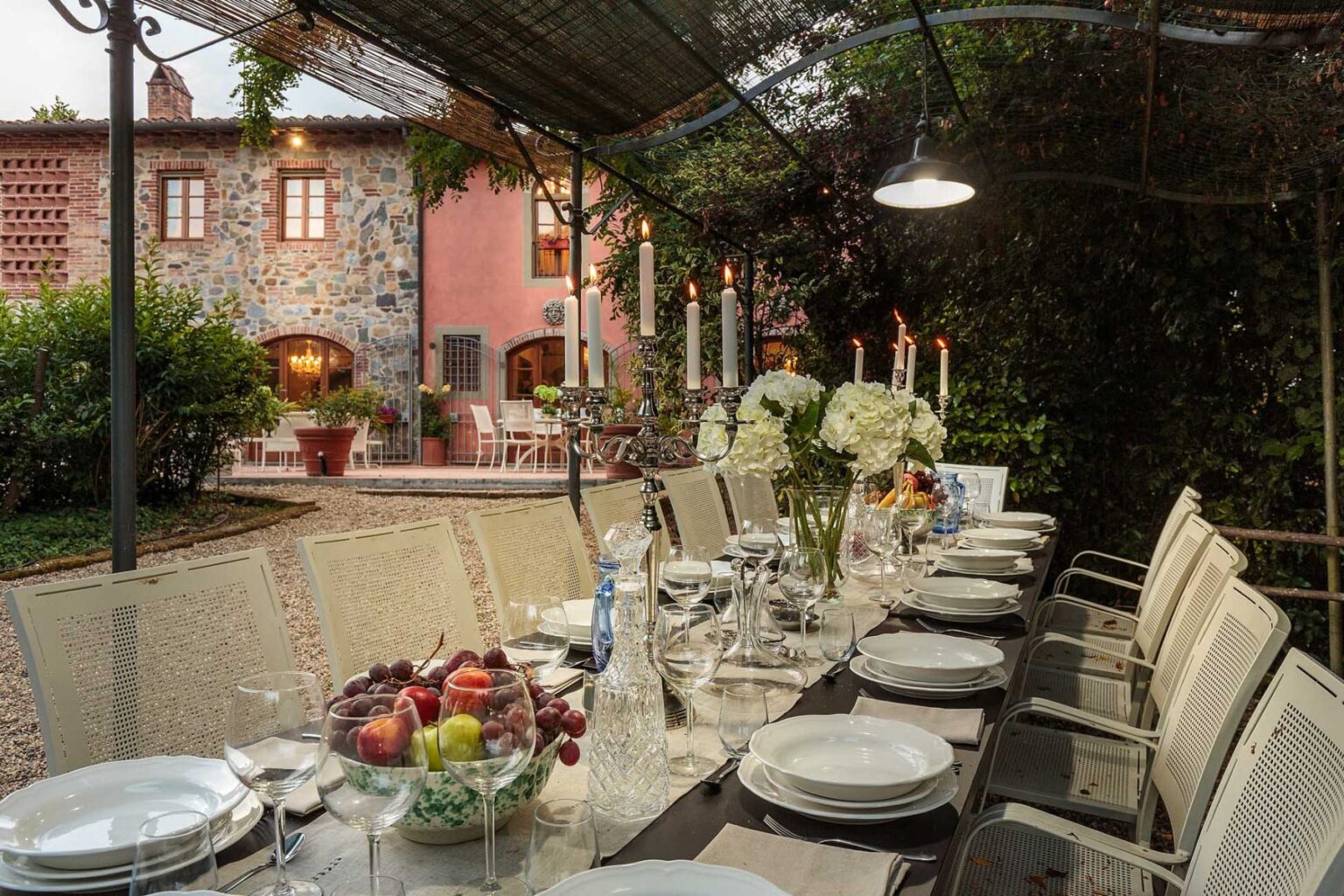 Elegant outdoor dining setup at a luxury villa in Italy, featuring a beautifully arranged table with fine china and a backdrop of lush gardens and classic architecture. Perfect for exclusive retreats and memorable gatherings. | Only on SopranoVillas