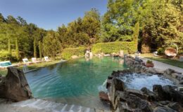 Scenic outdoor swimming pool surrounded by lush greenery, featuring natural rock formations and comfortable lounge chairs, ideal for relaxation and leisure.
