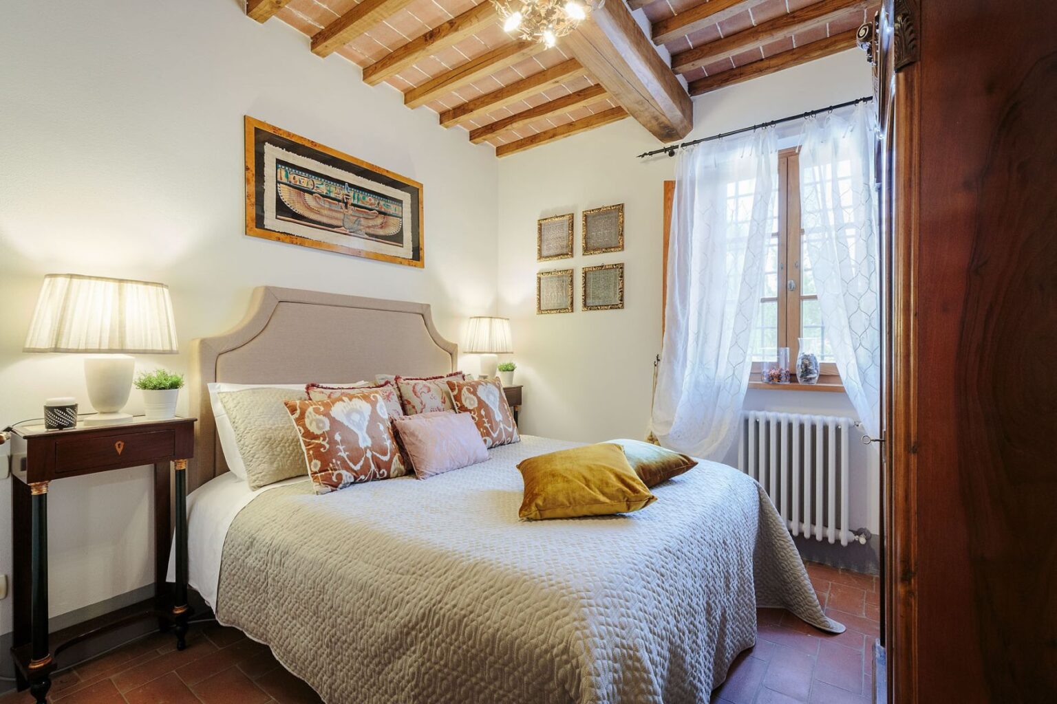 Cozy and elegantly decorated bedroom in a luxury villa for rent in Italy, featuring a comfortable bed, stylish lamps, and rustic wooden beams. Ideal for a relaxing getaway in a beautiful Italian setting. | Only on SopranoVillas