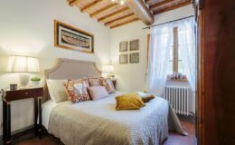 Cozy and elegantly decorated bedroom in a luxury villa for rent in Italy, featuring a comfortable bed, stylish lamps, and rustic wooden beams. Ideal for a relaxing getaway in a beautiful Italian setting.