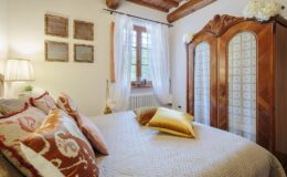 Cozy bedroom featuring a plush bed with decorative pillows, a wooden wardrobe, and soft lighting. The room has a rustic charm with exposed beams and elegant curtains, creating a warm and inviting atmosphere.