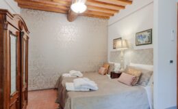 Cozy bedroom with two twin beds, wooden beams, and elegant decor, featuring a vintage wardrobe and soft lighting, ideal for relaxation and comfort.