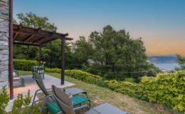 Scenic outdoor patio with lounge chairs and a small table, surrounded by lush greenery and overlooking a tranquil landscape at sunset. Ideal for relaxation and enjoying nature.