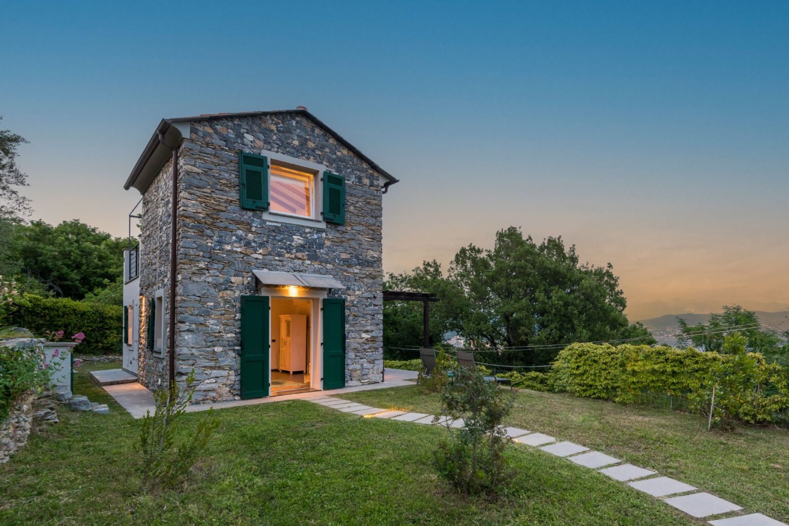 Charming stone house with green shutters and a welcoming entrance, surrounded by lush greenery and a pathway in a serene outdoor setting, perfect for a cozy getaway. | Only on SopranoVillas