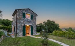 Charming stone house with green shutters and a welcoming entrance, surrounded by lush greenery and a pathway in a serene outdoor setting, perfect for a cozy getaway.