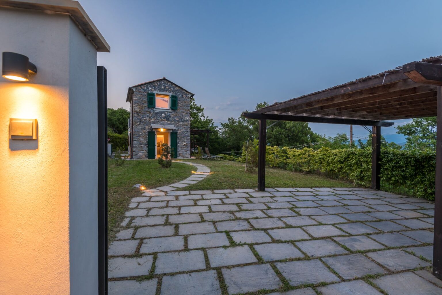 Stone cottage with green shutters surrounded by landscaped garden and pathway, featuring a wooden pergola, captured during twilight. | Only on SopranoVillas