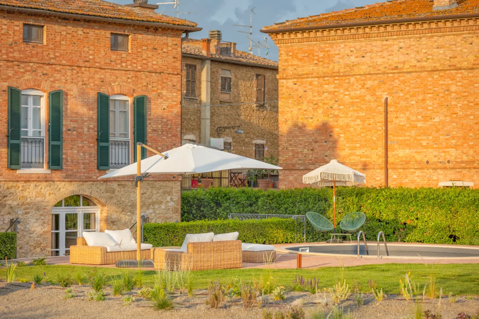 Cozy outdoor seating area with wicker furniture and umbrellas, surrounded by lush greenery and rustic brick buildings, ideal for relaxation in a scenic setting. | Only on SopranoVillas