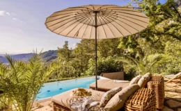 Luxurious outdoor lounge area featuring a large umbrella, comfortable seating, and a serene swimming pool with a scenic mountain backdrop, surrounded by lush greenery. Perfect for relaxation and enjoying nature.