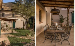 Charming outdoor dining area at a rustic Italian villa, featuring a wooden table set for a meal, surrounded by elegant metal chairs and lush greenery. The villa's facade is visible, showcasing a welcoming entrance and scenic landscaping. Perfect for al fresco dining experiences.