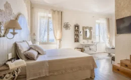 Bright and airy bedroom featuring a large bed with decorative pillows, elegant wall decor, and natural light streaming through sheer curtains. The room includes a vintage-style wash basin, a clawfoot bathtub, and tasteful furnishings, creating a serene and inviting atmosphere. Ideal for relaxation and comfort.