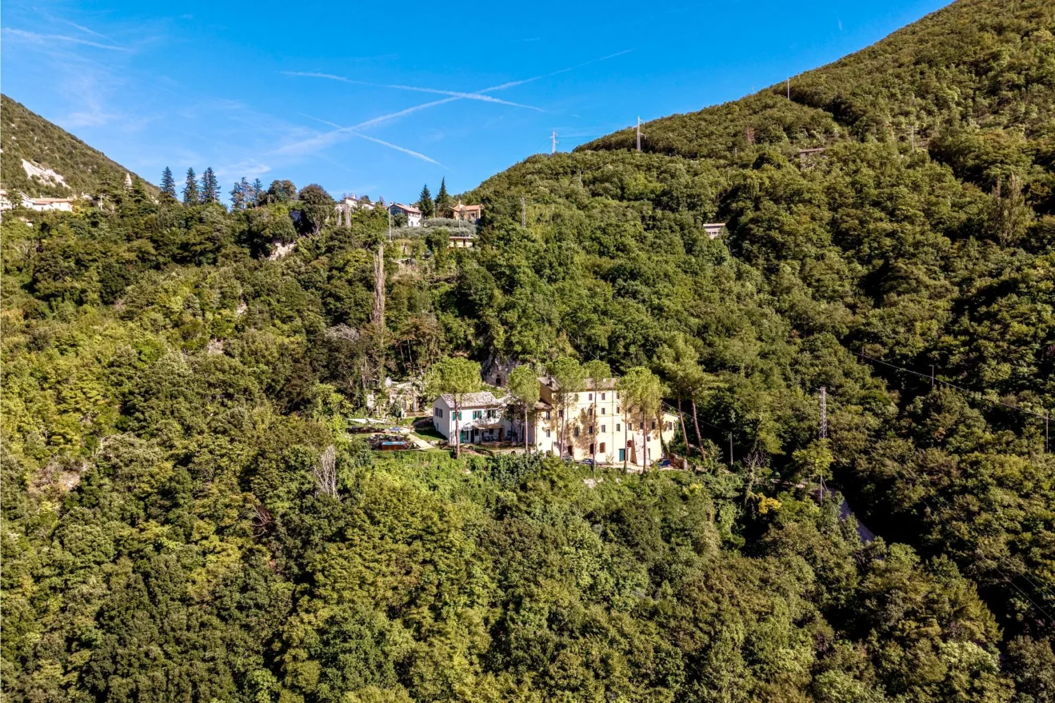 Aerial view of a secluded villa surrounded by lush greenery on a hillside, with clear blue skies and distant homes visible in the background. | Only on SopranoVillas