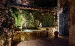 Serene garden water feature with cascading water, surrounded by lush green ivy and rustic stone walls, featuring a decorative statue and ambient lighting. Ideal for creating a tranquil outdoor retreat.