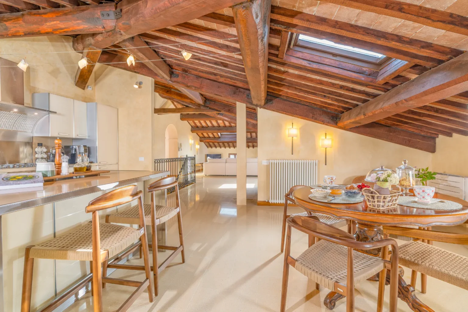 Bright and airy loft kitchen and dining area featuring exposed wooden beams, a modern kitchen island with bar stools, and a cozy dining table set for breakfast, showcasing a stylish interior design. | Only on SopranoVillas