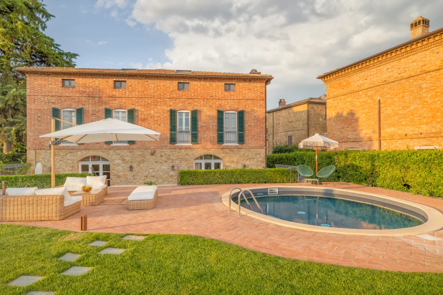 Charming rustic villa with a swimming pool, surrounded by lush greenery and a patio area featuring comfortable outdoor seating and an umbrella. The brick exterior showcases traditional architecture, while the tranquil setting offers a perfect retreat for relaxation. | Only on SopranoVillas