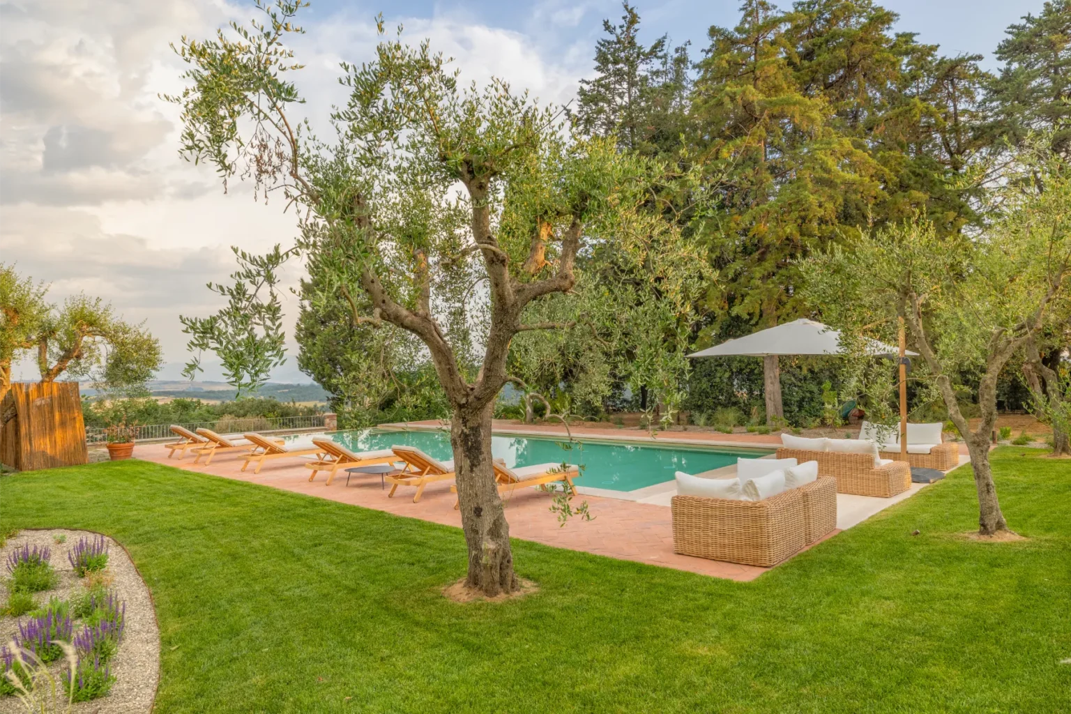 Luxurious outdoor pool area surrounded by olive trees and lush greenery, featuring comfortable lounge chairs and a shaded seating area, ideal for relaxation and enjoying nature. | Only on SopranoVillas