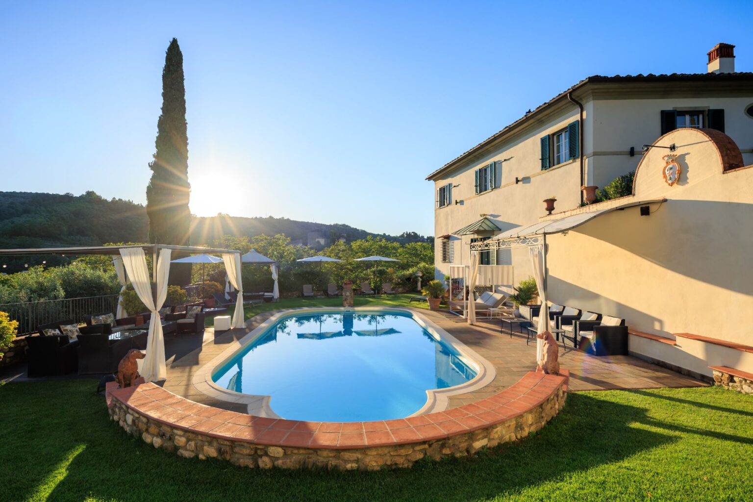 Luxurious villa with a swimming pool surrounded by lush greenery, featuring a sunset view, outdoor seating areas, and elegant architecture, perfect for relaxation and leisure. | Only on SopranoVillas