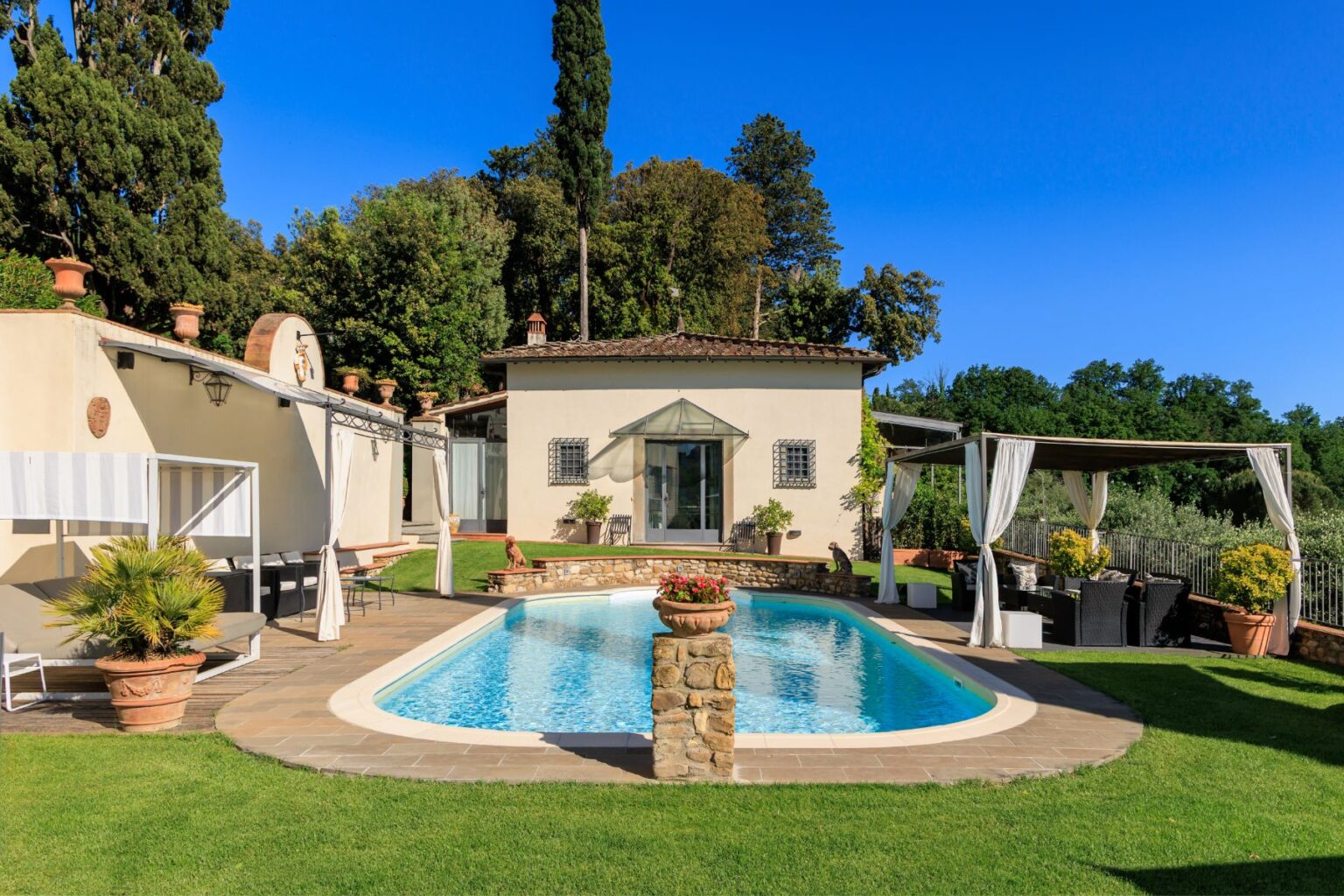 Beautiful Tuscan villa with a swimming pool surrounded by lush greenery, featuring a spacious patio area with seating and elegant canopies, ideal for relaxing and entertaining in a serene outdoor setting. | Only on SopranoVillas
