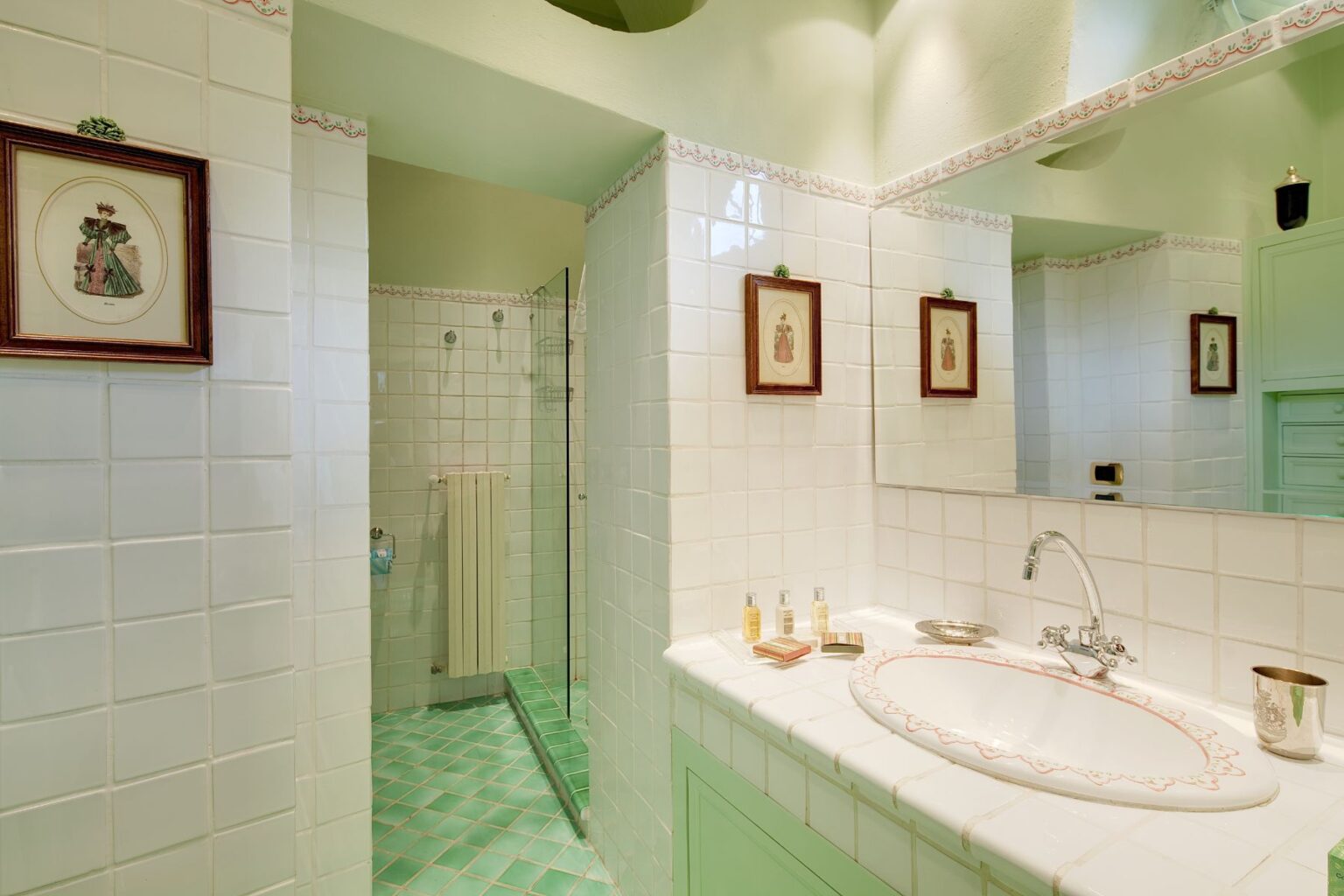 Bright and airy vintage-inspired bathroom featuring white tiled walls, mint green accents, and decorative framed artwork. The space includes a spacious shower, a stylish sink with an elegant faucet, and neatly arranged toiletries on the countertop. | Only on SopranoVillas