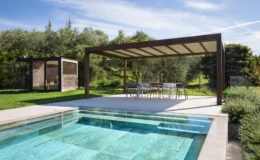 Modern outdoor space featuring a swimming pool, shaded dining area under a pergola, and a wooden garden shed surrounded by lush greenery. Ideal for relaxation and entertaining in a serene environment.