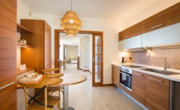 Modern kitchen interior featuring wooden cabinetry, a stylish pendant light, and a cozy dining area with a round table and chairs. The space is bright and open, showcasing contemporary design elements and a clean, functional layout.