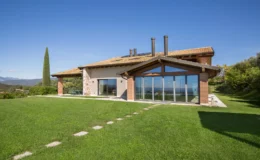 Modern hillside villa featuring large glass windows, a sloped roof, and a spacious lawn with stone pathway, surrounded by lush greenery and mountain views. Perfect for luxury living and outdoor relaxation.