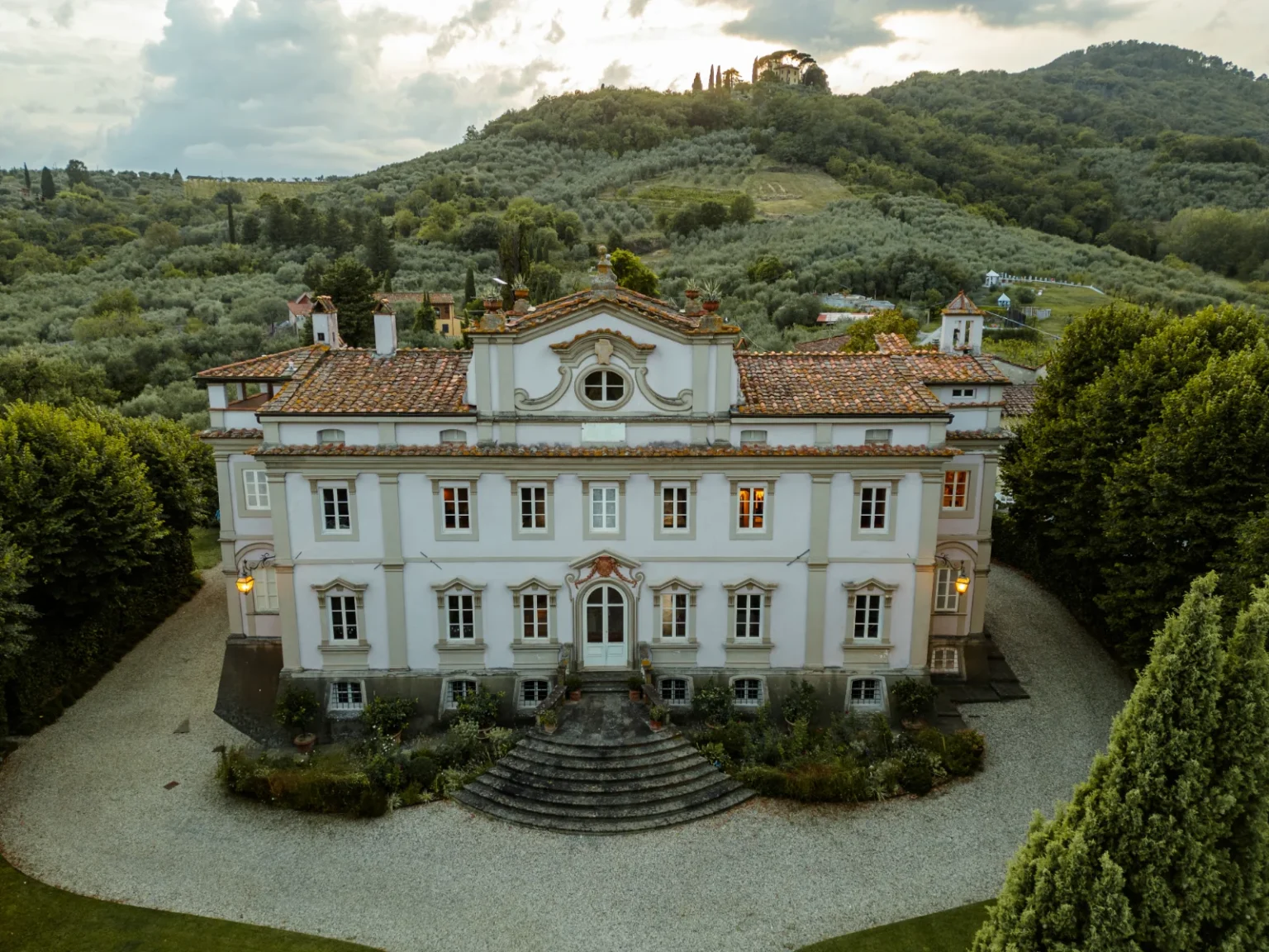 Elegant villa surrounded by lush greenery in a serene landscape, featuring a classic architectural design with a tiled roof and well-maintained gardens. | Only on SopranoVillas