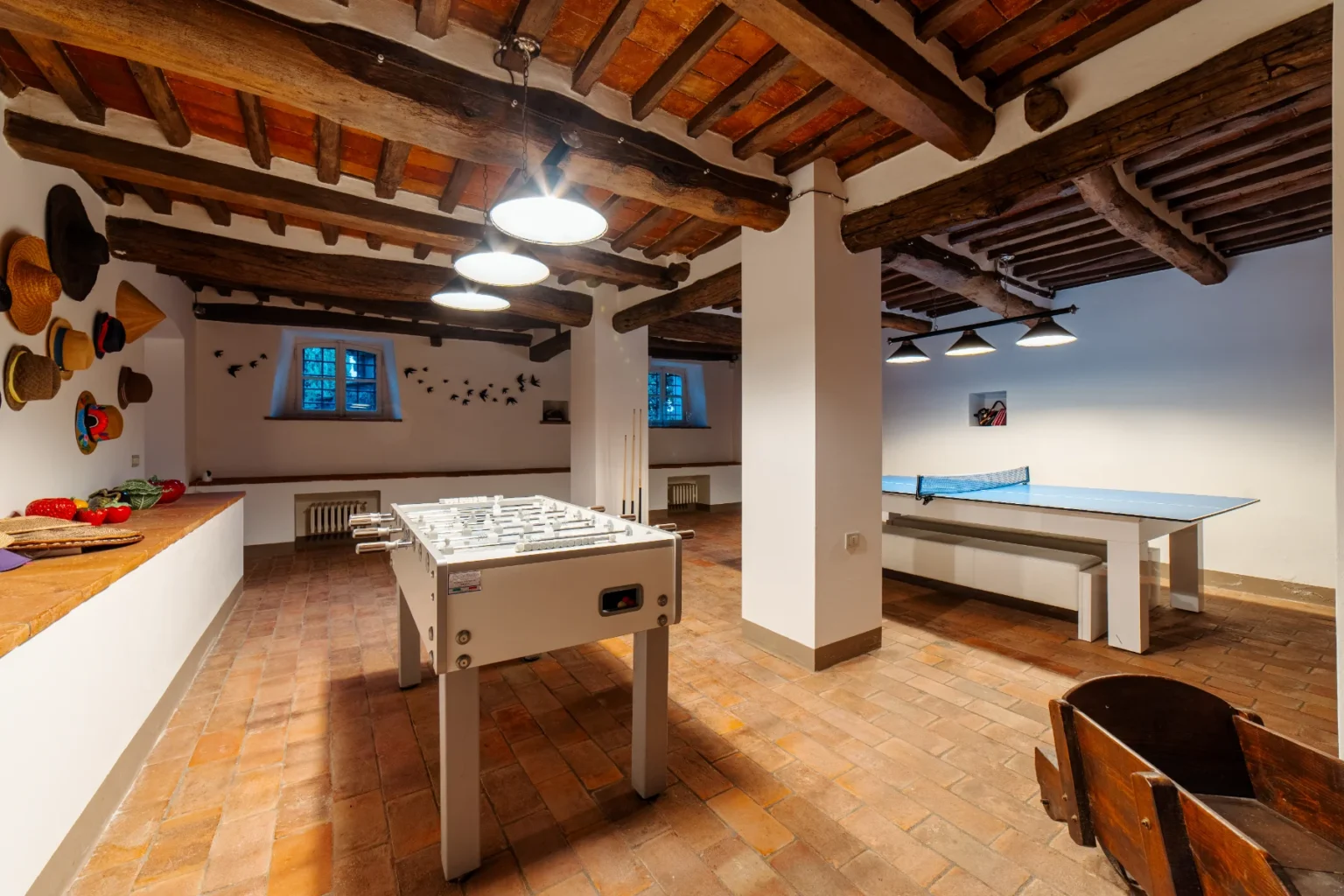 Recreational room featuring a foosball table, a ping pong table, and decorative hats on the wall, set in a space with exposed wooden beams and terracotta flooring, ideal for leisure activities. | Only on SopranoVillas