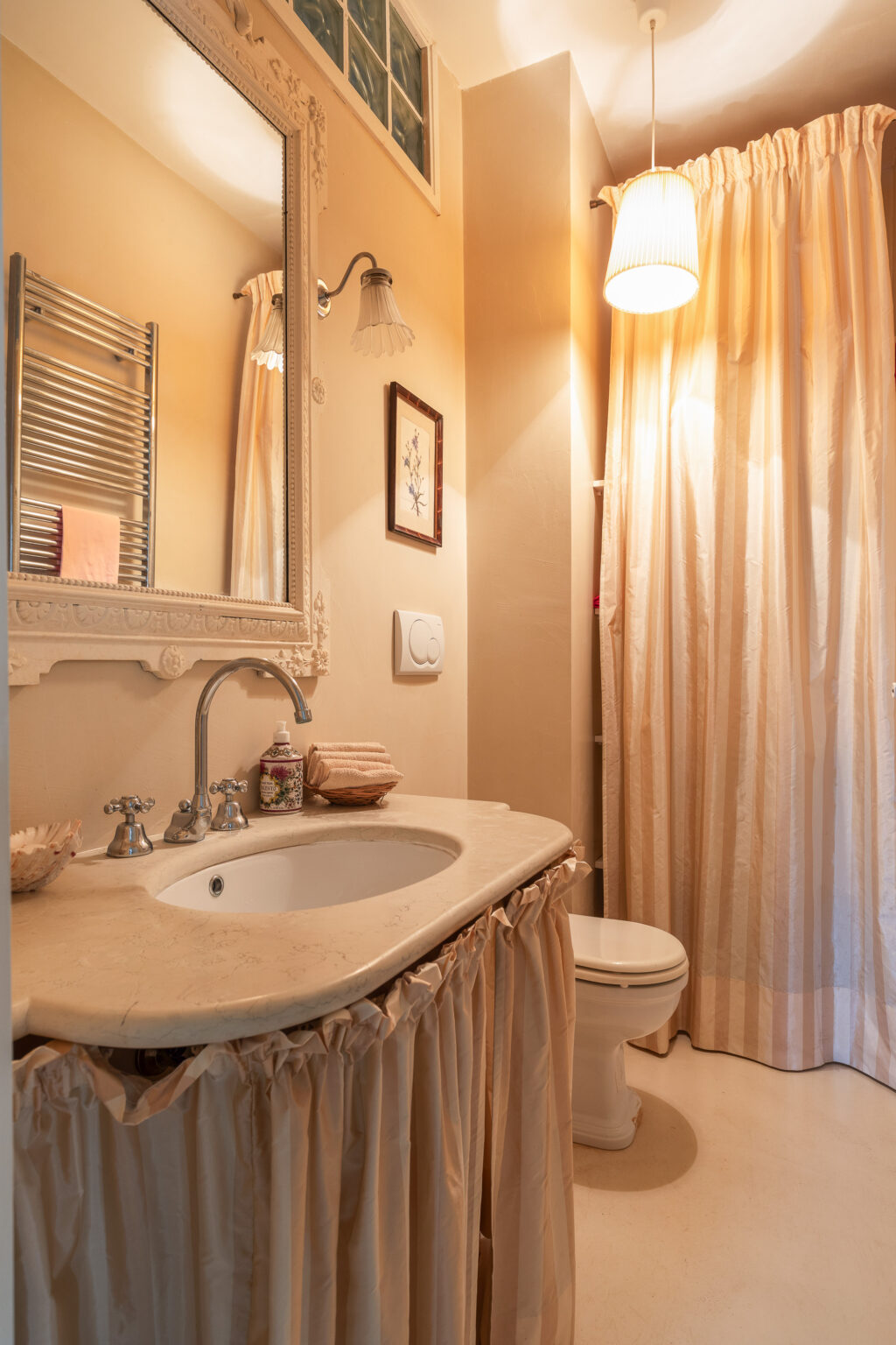 Elegant bathroom interior featuring a marble sink with vintage-style faucets, a decorative mirror, and warm lighting. The space includes a shower curtain, a towel rack, and neatly arranged toiletries, creating a cozy and inviting atmosphere. | Only on SopranoVillas