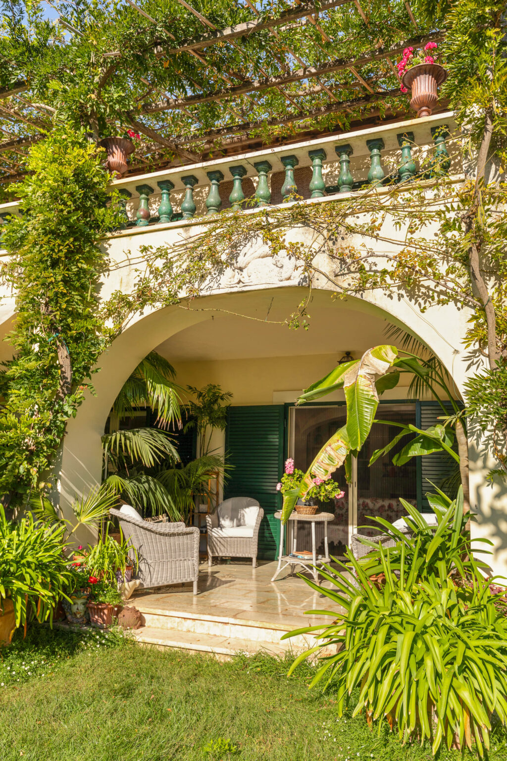 Charming outdoor patio area with wicker chairs and lush greenery, featuring a decorative balcony with potted plants and vines, creating a serene and inviting atmosphere. | Only on SopranoVillas