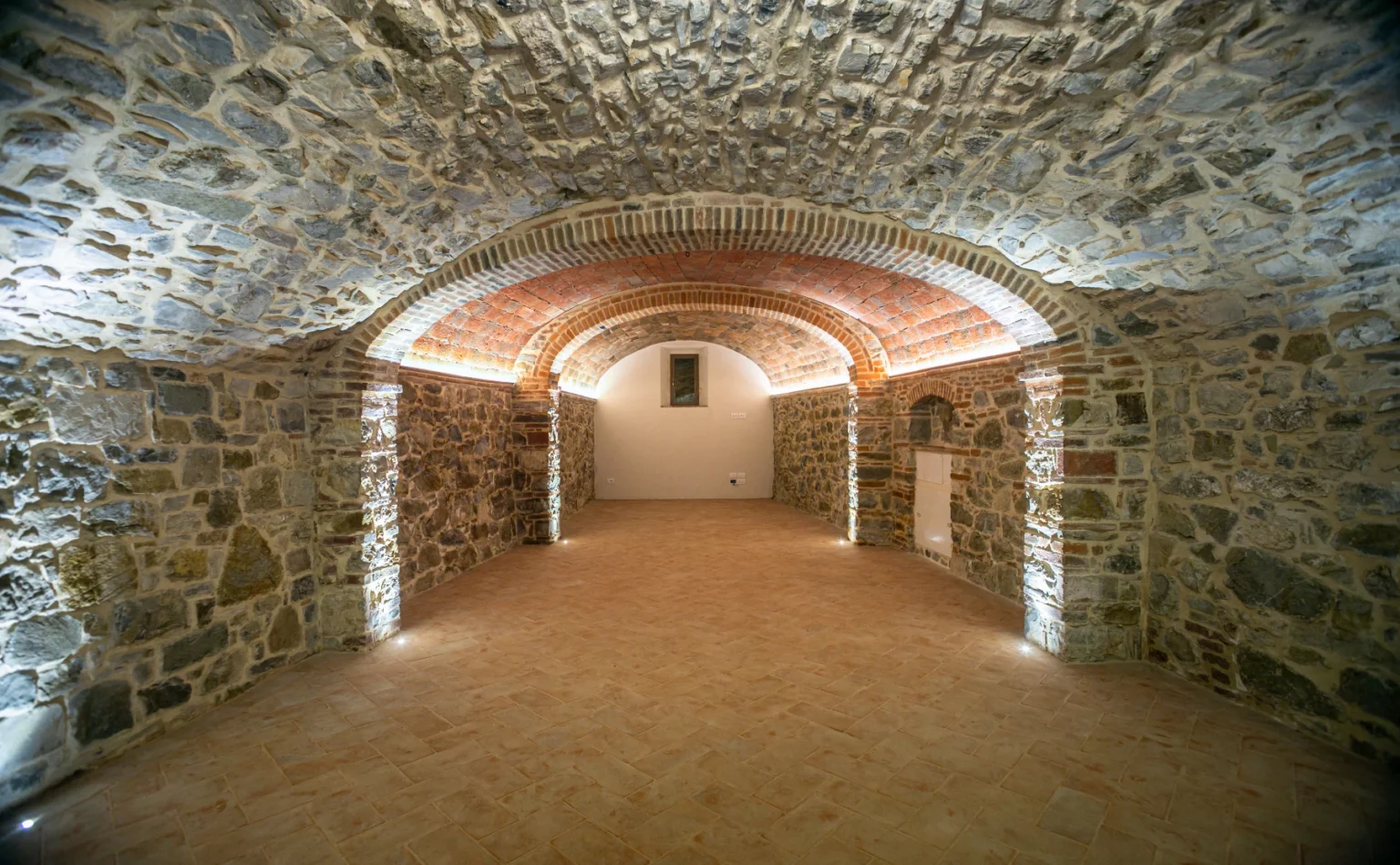 Spacious underground cellar featuring arched stone walls and modern lighting, ideal for wine storage or event space. | Only on SopranoVillas