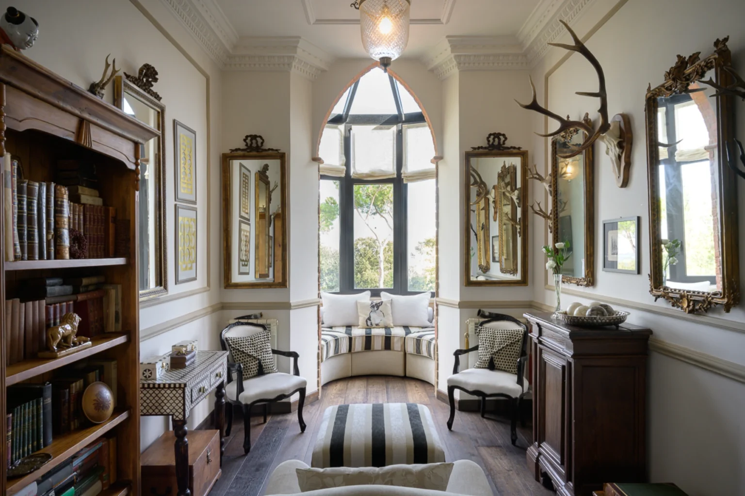 Elegant interior design of a cozy sitting area featuring vintage furniture, decorative mirrors, and a charming bay window. The space is adorned with bookshelves, patterned cushions, and rustic accents, creating a warm and inviting atmosphere. | Only on SopranoVillas