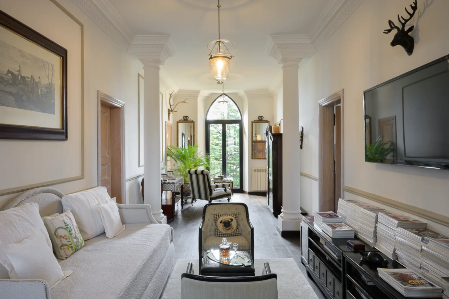 Elegant hallway interior featuring plush seating, decorative artwork, and tall windows that invite natural light. The space is adorned with classic furnishings, including a stylish coffee table and a mix of modern and traditional decor elements. | Only on SopranoVillas