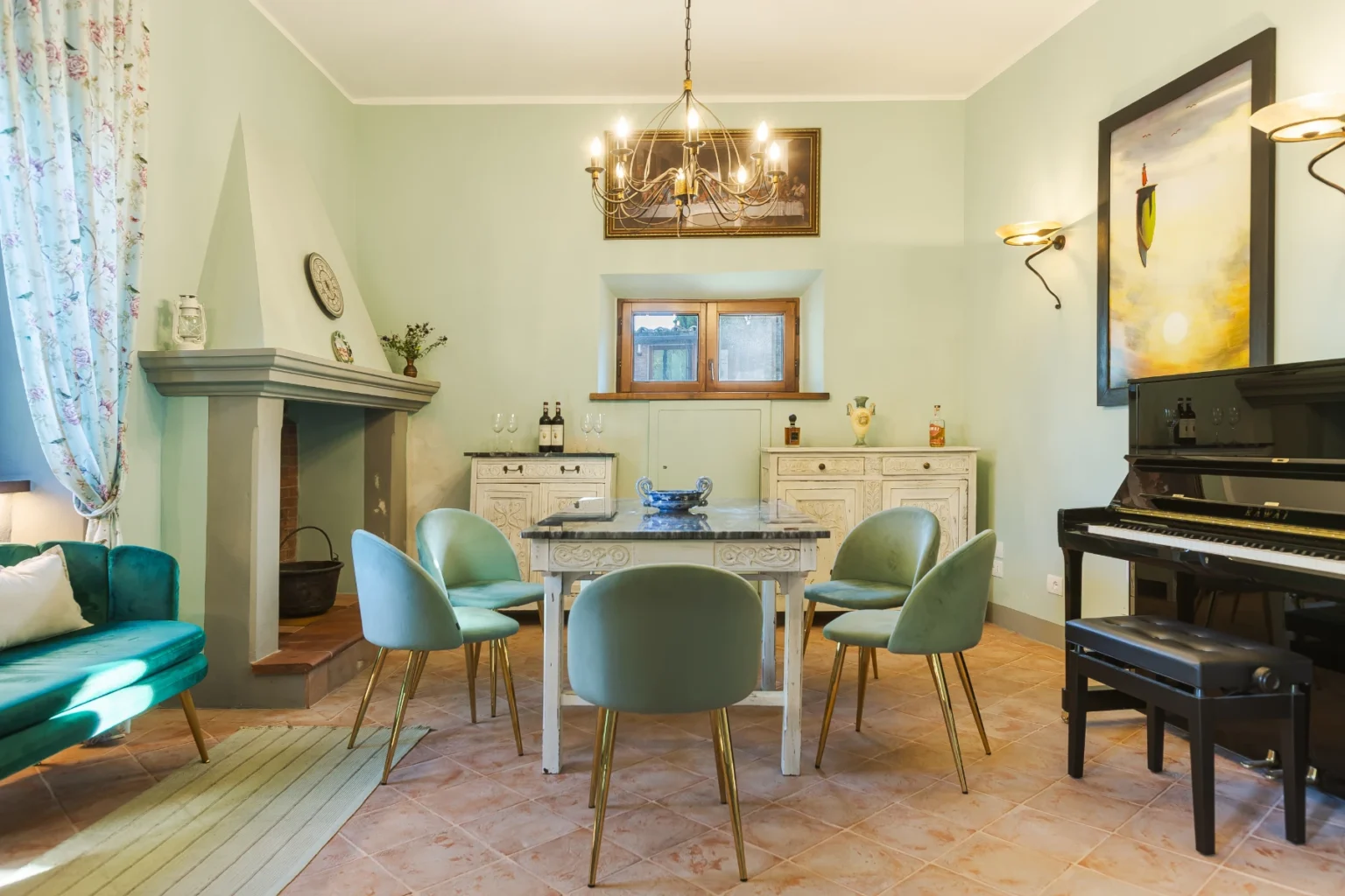 Elegant dining room featuring a vintage table surrounded by mint green chairs, a cozy fireplace, and a grand piano. Soft pastel walls and decorative curtains create a warm ambiance, complemented by stylish lighting fixtures and artistic decor. Ideal for intimate gatherings and family meals. | Only on SopranoVillas