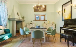Elegant dining room featuring a vintage table surrounded by mint green chairs, a cozy fireplace, and a grand piano. Soft pastel walls and decorative curtains create a warm ambiance, complemented by stylish lighting fixtures and artistic decor. Ideal for intimate gatherings and family meals.