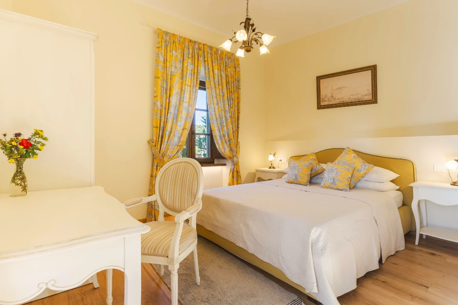 Cozy bedroom featuring a yellow and white color scheme, a queen-sized bed with decorative pillows, a vintage-style desk and chair, and elegant yellow curtains. The room is well-lit with natural light and includes a vase of fresh flowers, creating a warm and inviting atmosphere. | Only on SopranoVillas