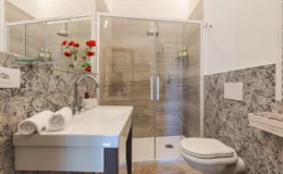 Modern bathroom featuring a glass shower enclosure, sleek sink with decorative towels, and stylish wall tiles. The space is enhanced by vibrant red flowers, creating a fresh and inviting atmosphere.