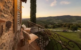 Scenic balcony view overlooking rolling hills and vineyards at sunset, featuring rustic stone walls, elegant seating, and lush greenery in a tranquil countryside setting.