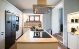 Modern kitchen featuring sleek stainless steel appliances, a spacious island with an induction cooktop, and stylish cabinetry. Natural light streams through the window, illuminating the elegant countertop and decorative backsplash.
