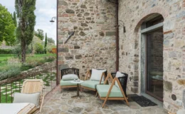 Outdoor seating area featuring modern chairs and a small table, set against a rustic stone wall with lush greenery in the background. Ideal for relaxation in a tranquil garden setting.