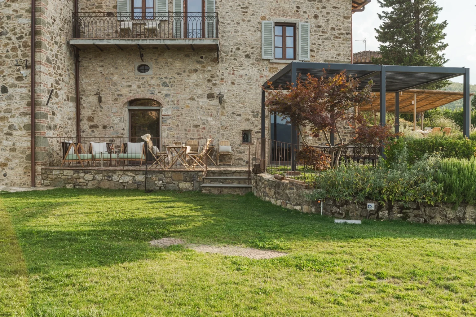 Rustic stone villa with a spacious garden, featuring a wooden terrace with seating and a covered outdoor dining area surrounded by greenery. Ideal for relaxation and outdoor entertaining. | Only on SopranoVillas