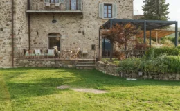 Rustic stone villa with a spacious garden, featuring a wooden terrace with seating and a covered outdoor dining area surrounded by greenery. Ideal for relaxation and outdoor entertaining.